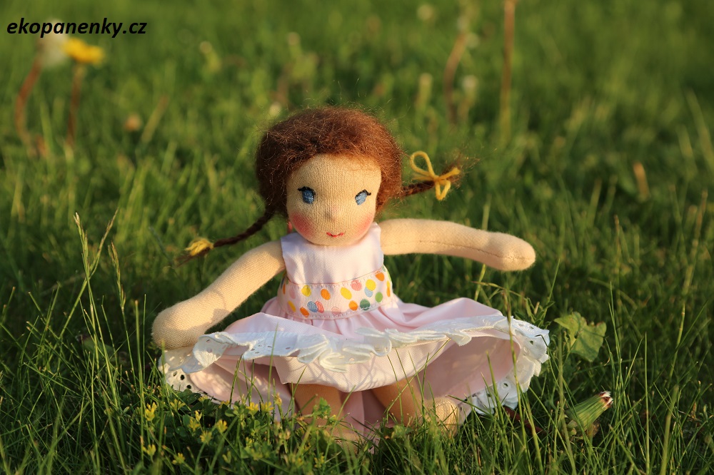 ručně šitá sváteční panenka v růžových šatičkách sedí v trávě