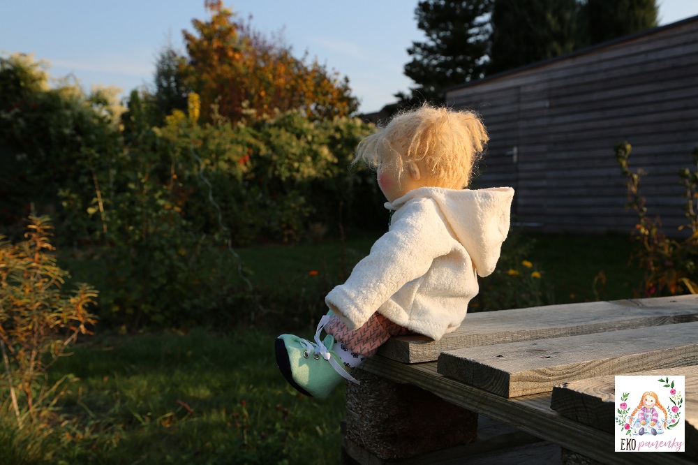 Sladká holčička, waldorfská panenka batole sedící v kabátku na zahradě, ekopanenky